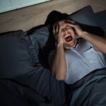 Homem acorda gritando e com as mãos no rosto, ilustrando a angústia de sonhos com a morte