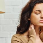 Mulher com olhos fechados toca o pescoço para indicar possíveis sintomas de doenças na tireoide
