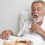 Homem idoso faz refeição no leito para ilustrar a rotina de alimentação para idosos acamados.