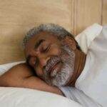 Homem idoso dorme tranquilamente na cama para ilustrar a importância do sono na terceira idade.